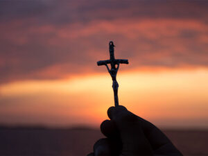 Una mano sostiene una cruz con el atardecer de fondo